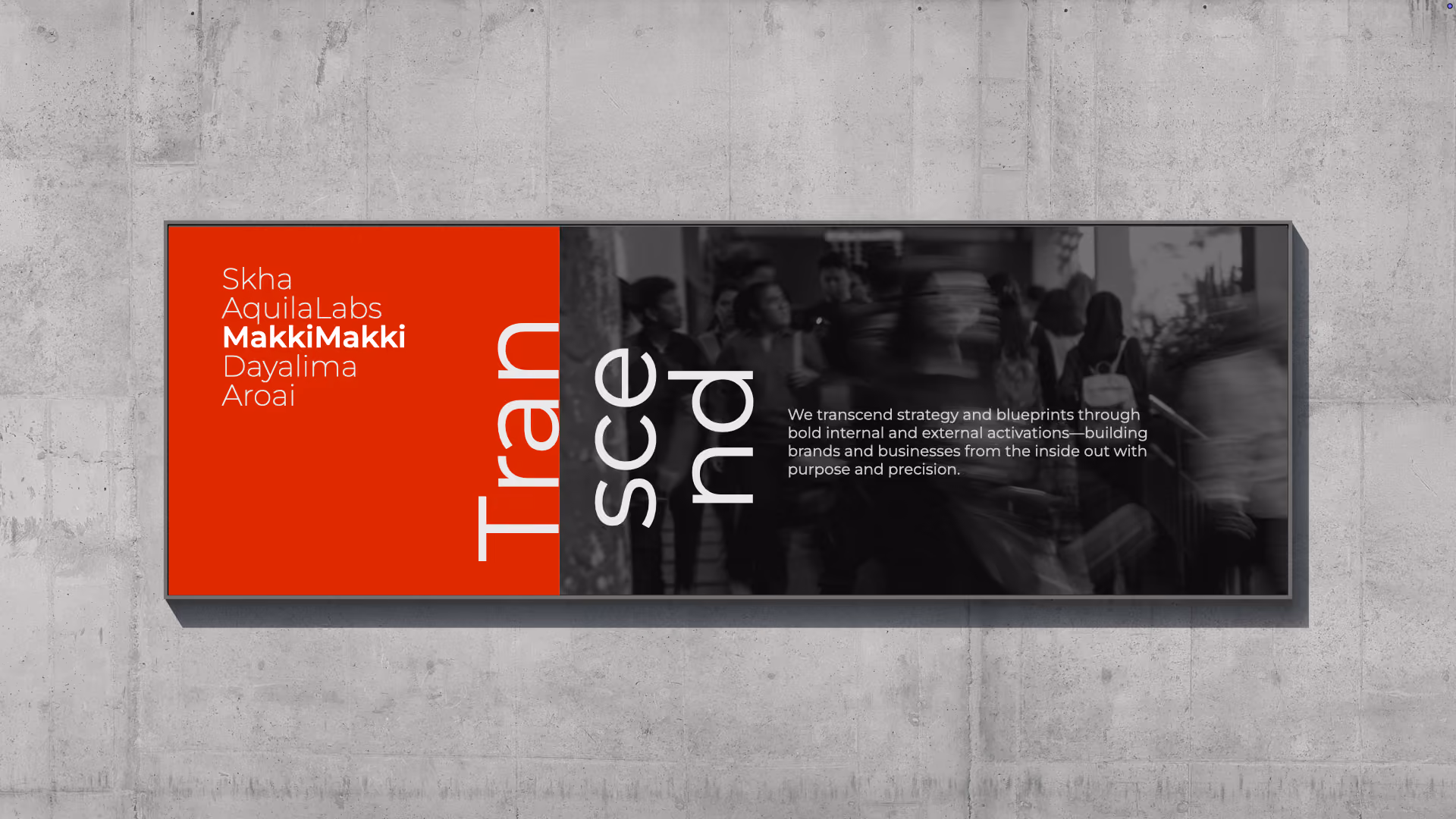 A rectangular wall sign with a red section on the left listing names: Skha, AquilaLabs, MakkiMakki (bolded), Dayalima, Aroai, and a black and white blurred background photo of people on the right with large white vertical text reading 'Transcend' split across three lines. Smaller white text says: 'We transcend strategy and blueprints through bold internal and external activations—building brands and businesses from the inside out with purpose and precision.'